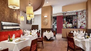 A restaurant with multiple tables set for dining, a bar area, and a red upholstered seating area. - DoubleTree by Hilton New York Downtown (New York)