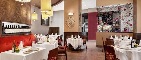 A restaurant with multiple tables set for dining, a bar area, and a red upholstered seating area.