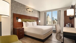 A hotel room with a large bed, a desk, a chair, and a view of a cityscape through the window. - DoubleTree by Hilton New York Downtown (New York)