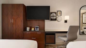 Ein Hotelzimmer mit einem Bett, einem Schreibtisch mit Stuhl, einem Kleiderschrank, einem Flachbildfernseher, einer Kaffeemaschine und einer Wandleuchte.