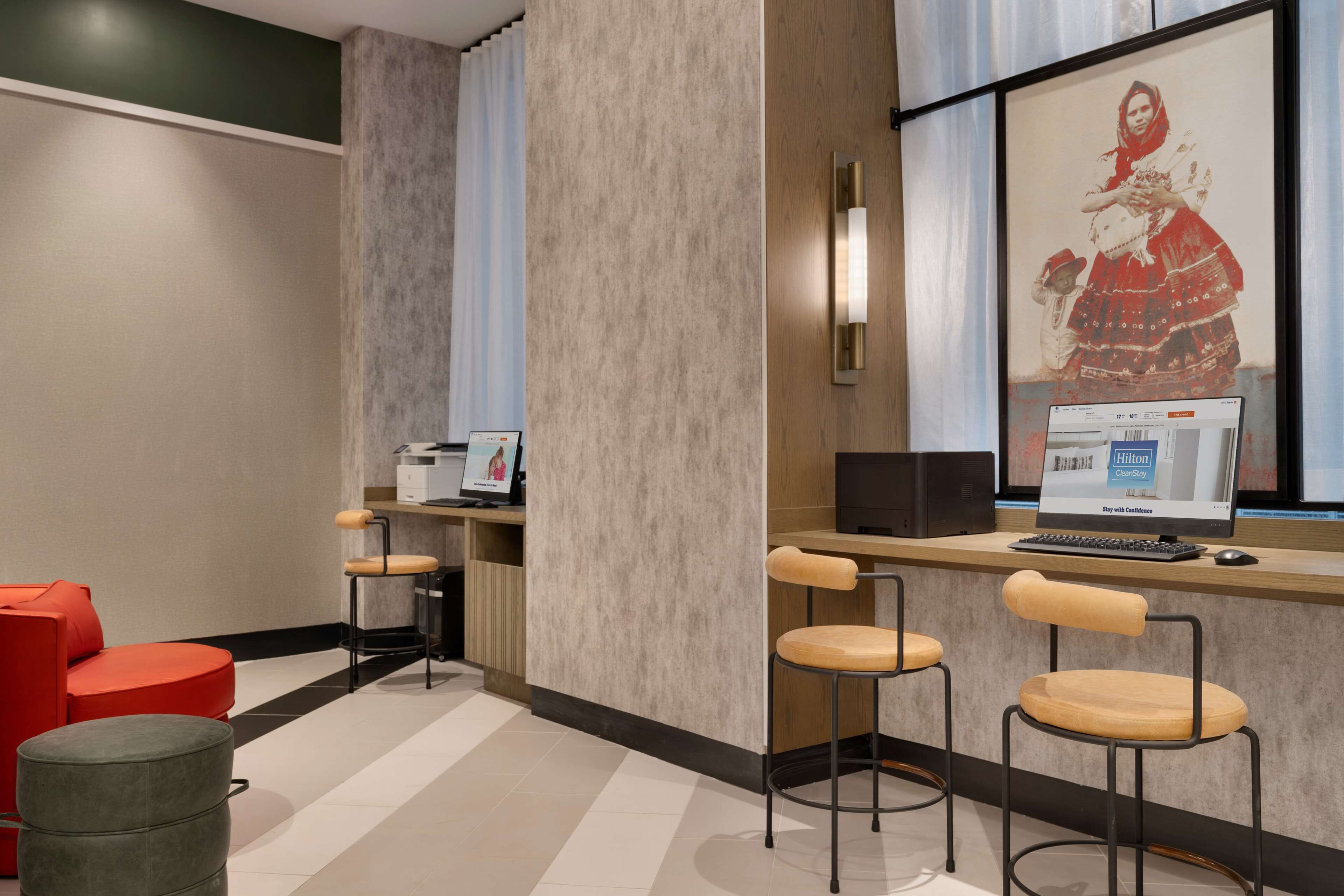 A modern hotel lobby with a reception desk, two bar stools, a red sofa, and a large framed picture on the wall.