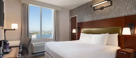 A hotel room with a large bed, a desk with a chair, a TV, and a window with curtains.