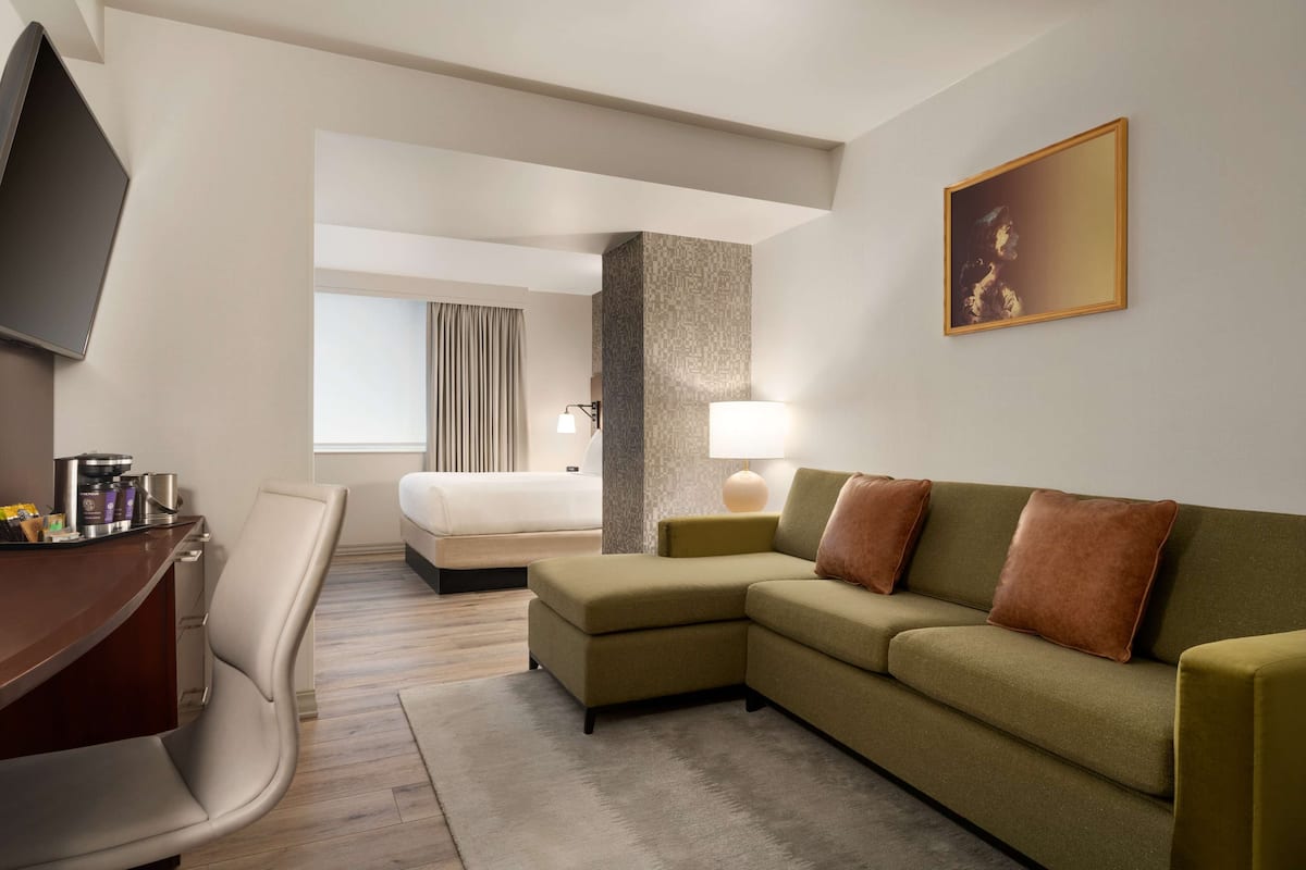 Hotellihuone, jossa on sohva, työpöytä, tuoli, sänky, televisio, lamppu ja taulu seinällä.