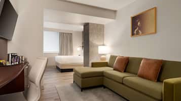 Una camera d'albergo con divano, scrivania, sedia, letto, televisione, lampada e un quadro appeso al muro.