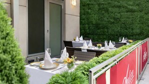 An outdoor dining area with tables set for two, featuring white tablecloths, gold and white napkins, and glassware. - DoubleTree by Hilton New York Downtown (New York)