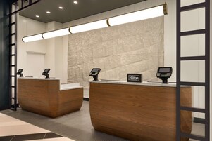 Uma área de recepção de hotel com dois balcões de madeira, uma parede de mármore e uma luminária moderna.
