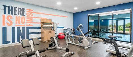 A gym with various exercise equipment, a motivational wall, and a view of the outdoors.