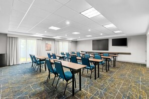 Una sala de conferencias con mesas y sillas, una pantalla grande y un piso con diseño.