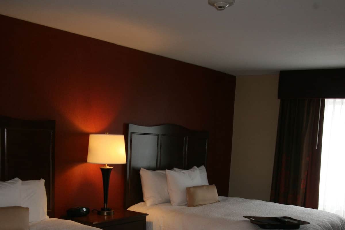 A hotel room with two beds, a nightstand with a lamp, and a headboard.
