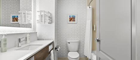 A modern bathroom with a white sink, a wooden vanity, a toilet, and a shower curtain.