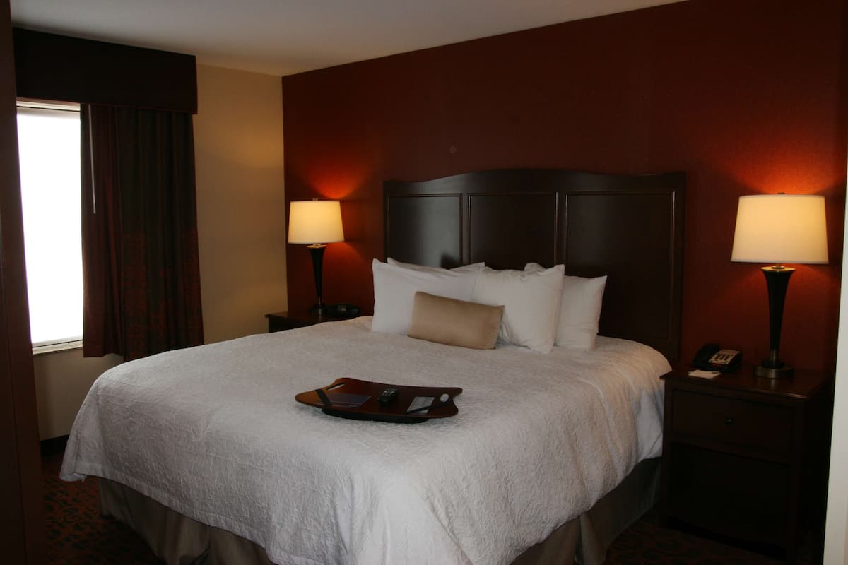 A hotel room with a large bed, two bedside lamps, a tray with a laptop, and a telephone on the nightstand.