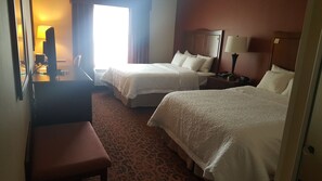 Habitación de hotel con dos camas, un escritorio, una silla y una lámpara.