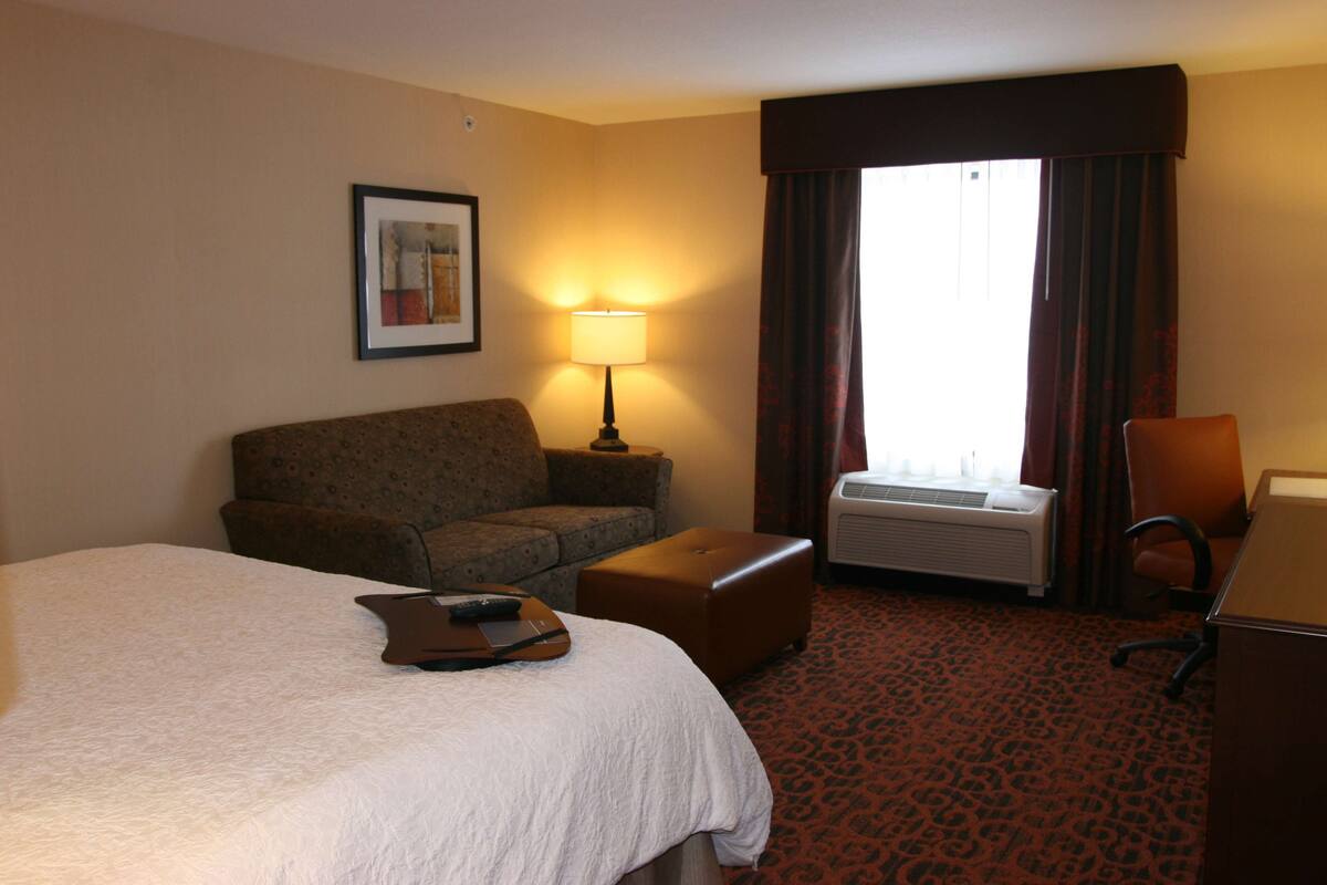 A hotel room with a large bed, a sofa, a desk, and a window with curtains.