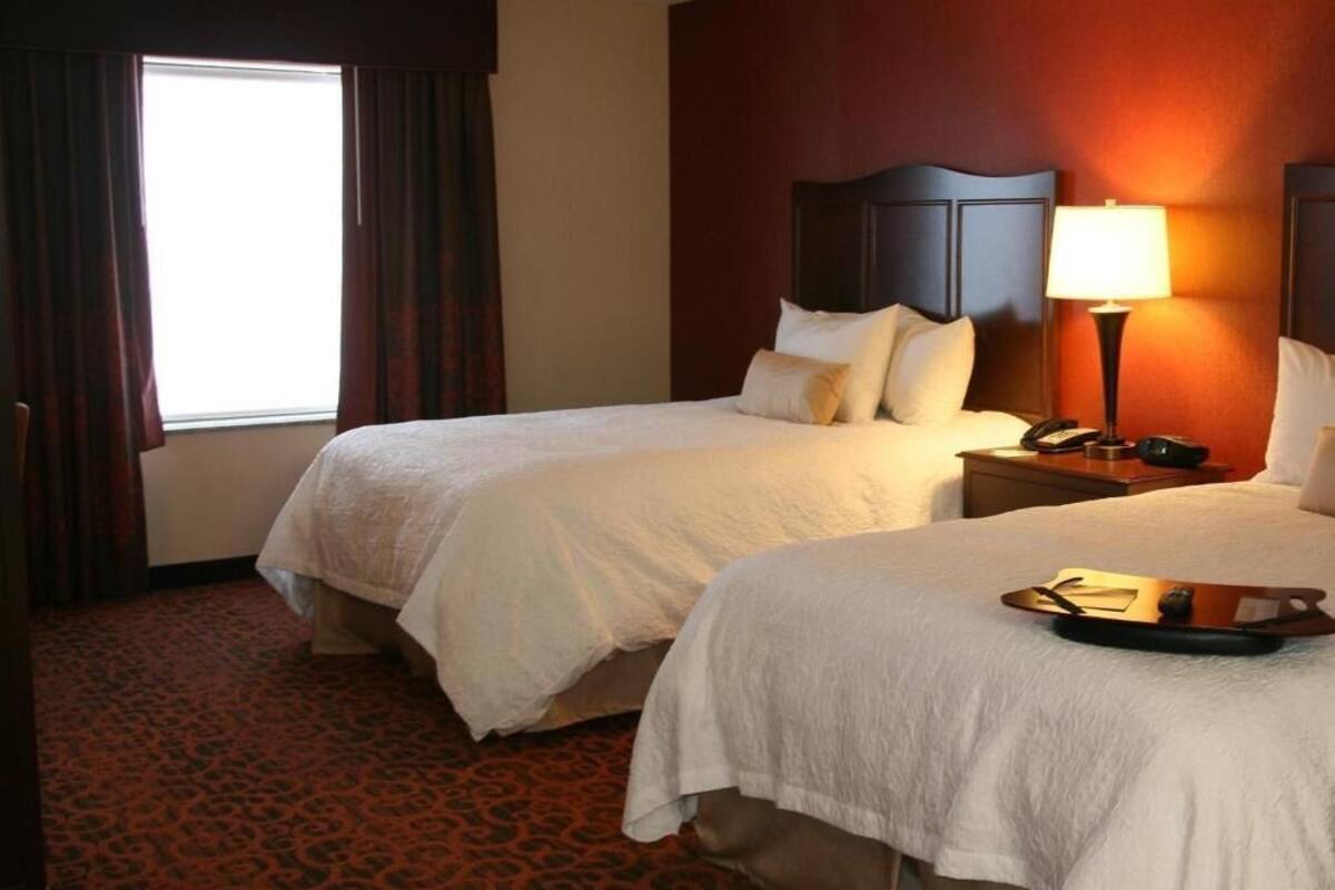 Une chambre d’hôtel avec deux lits, une table de chevet avec une lampe, un téléphone et un plateau avec un livre.