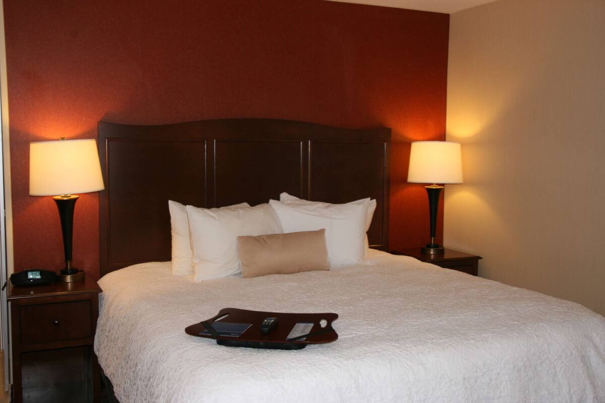A neatly made bed with a tray of items, two bedside lamps, and a dark headboard in a hotel room.