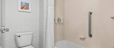 Une salle de bain comprenant des toilettes, une douche équipée d’une barre d’appui et une baignoire.