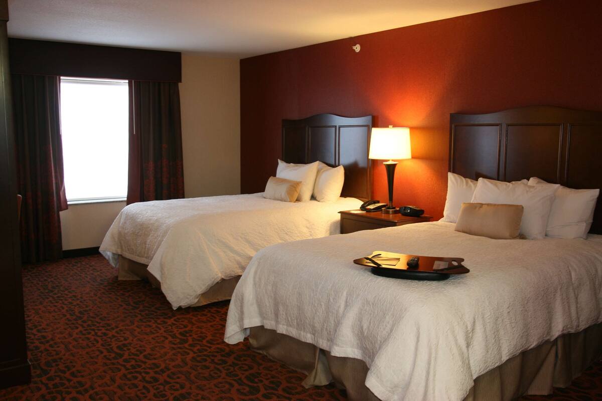 A hotel room with two beds, a red carpet, and a window with curtains.