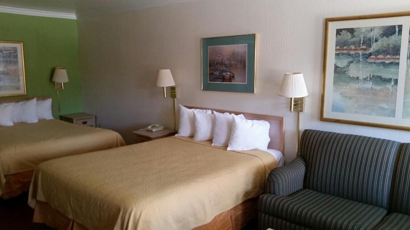 A hotel room with two beds, a sofa, and artwork on the walls.