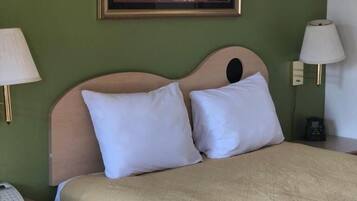 Une chambre d’hôtel comprenant un lit, deux lampes de chevet, une table de chevet avec un téléphone et une télécommande, une chaise et une œuvre d’art encadrée accrochée au mur.