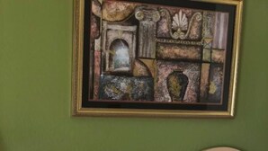 Uma cama com cabeceira bege e duas almofadas brancas, um edredom estampado e uma obra de arte emoldurada acima da cama.