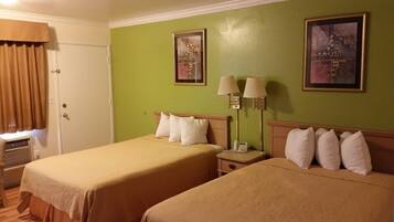 A hotel room with two beds, a door, a window with curtains, and two wall-mounted lamps.
