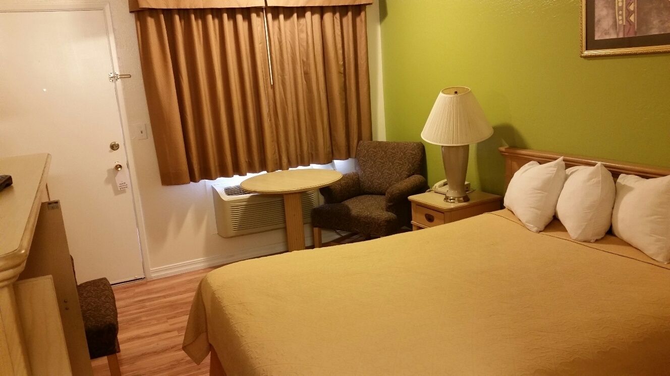 Habitación de hotel con una cama, una silla, una mesita, una lámpara y una ventana con cortinas.