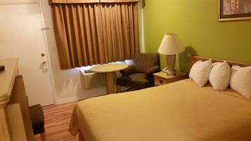 Habitación de hotel con una cama, una silla, una mesita, una lámpara y una ventana con cortinas.