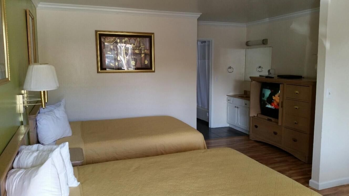 A hotel room with two beds, a TV, a dresser, and a framed picture on the wall.