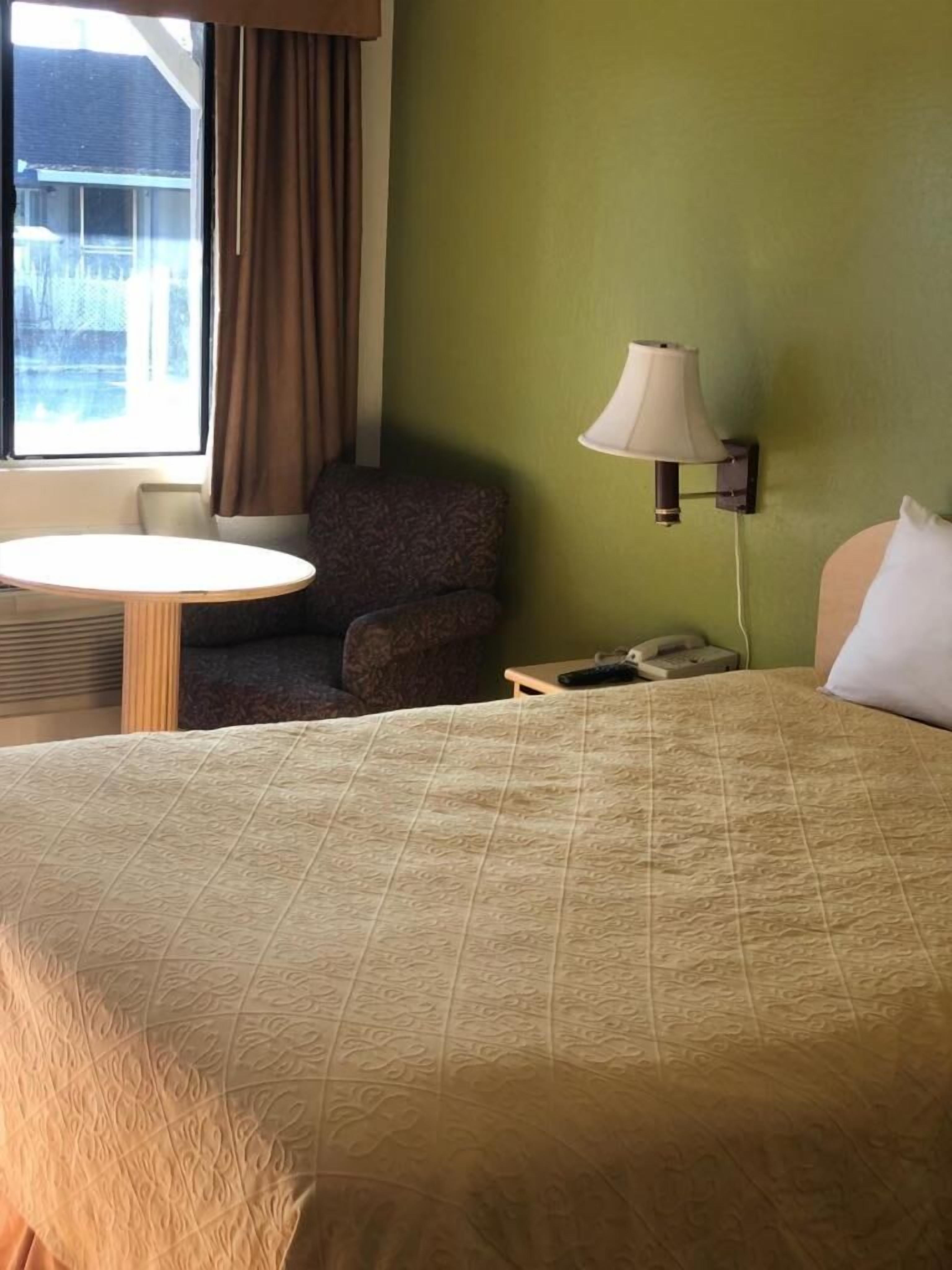 Et hotelværelse med en seng, en stol, et lille bord, en lampe og udsigt udad.