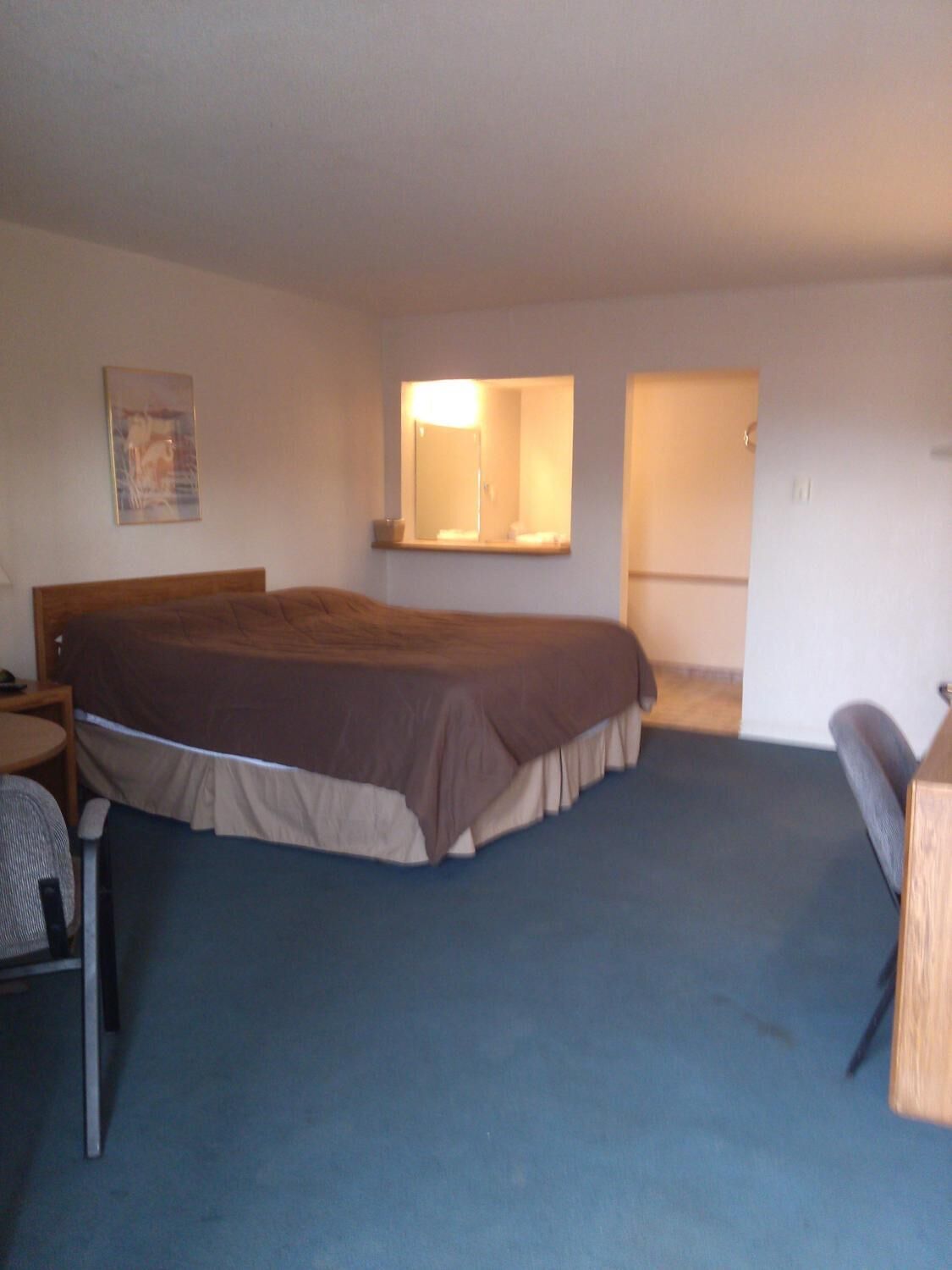 Ein Schlafzimmer mit einem Einzelbett, einem Schreibtisch, einem Stuhl, einem Spiegel und einer Tür zu einem anderen Raum.