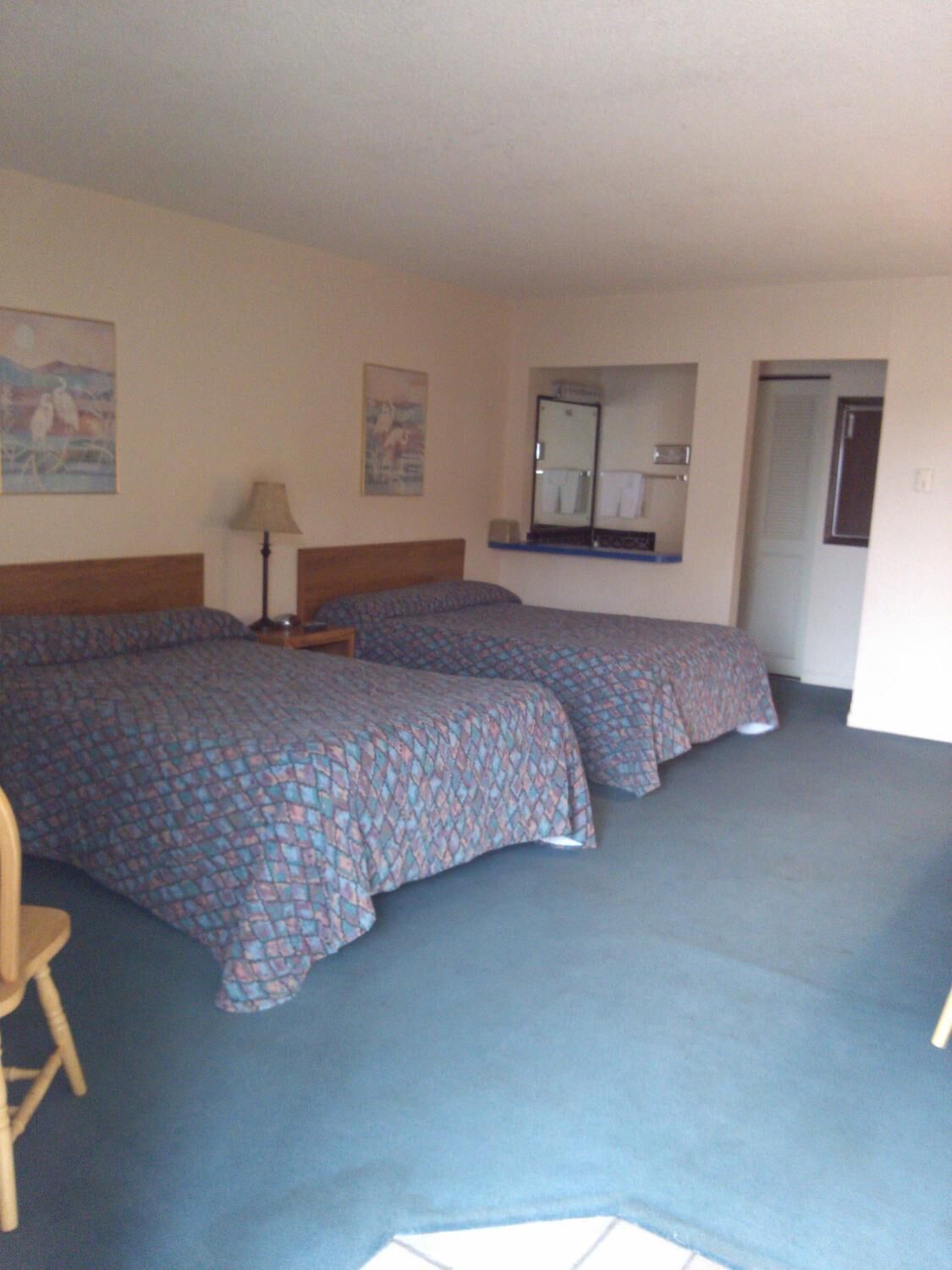 A hotel room with two beds, a wooden chair, a lamp, and a mirror.
