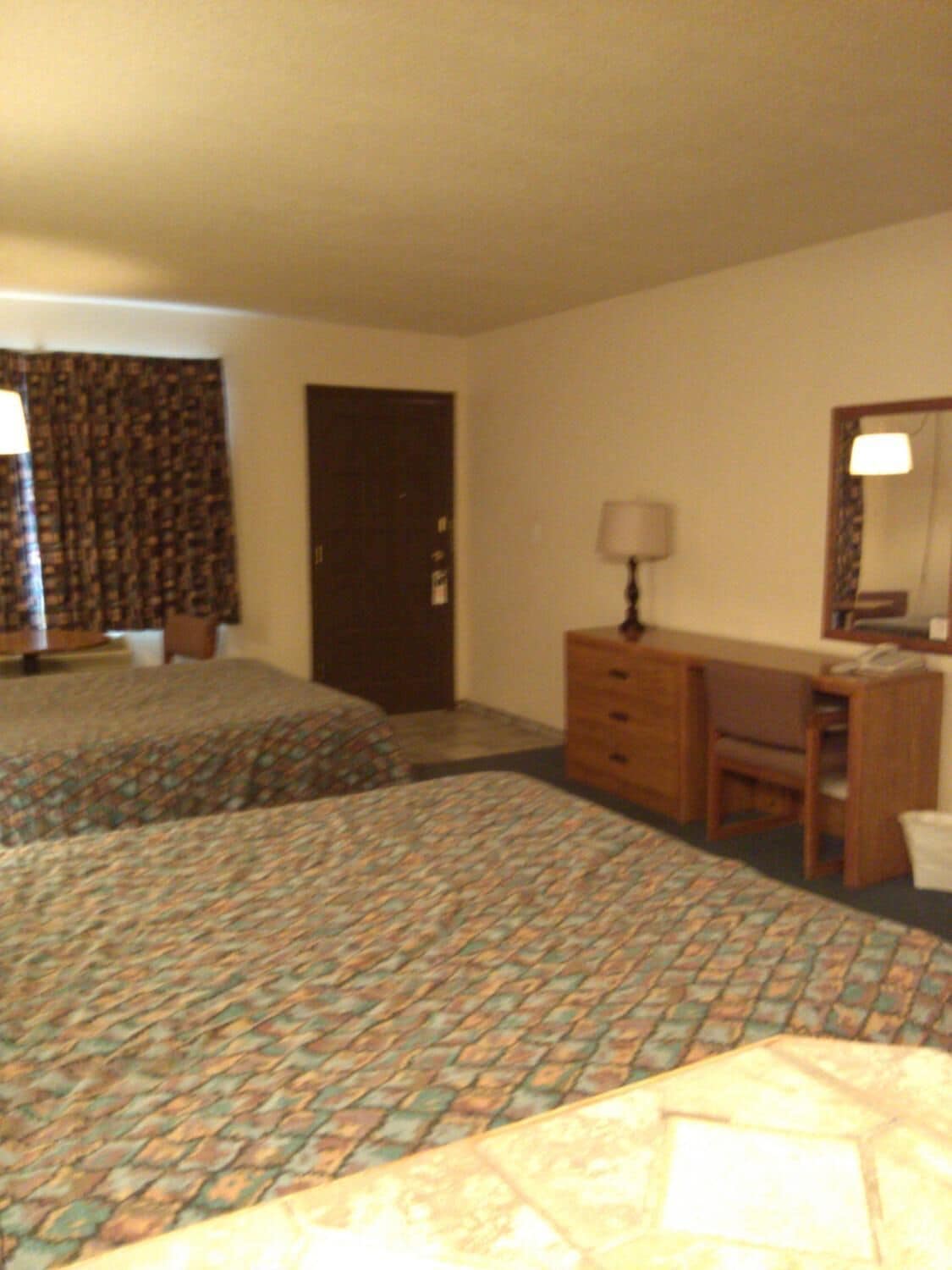 Habitación de hotel con dos camas, un escritorio, una silla, un aparador y una puerta.