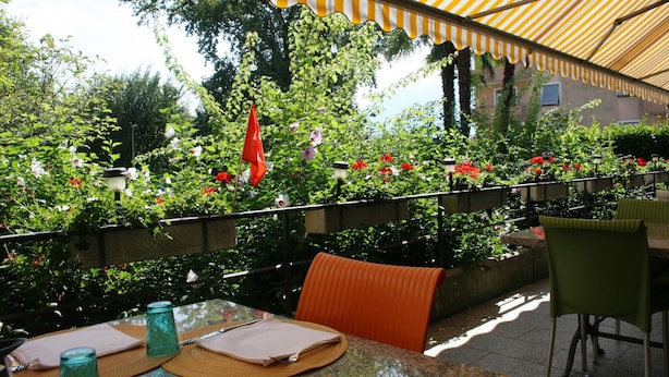 An outdoor patio with tables and chairs, surrounded by lush greenery and flowering plants. - Rovere (Losone)