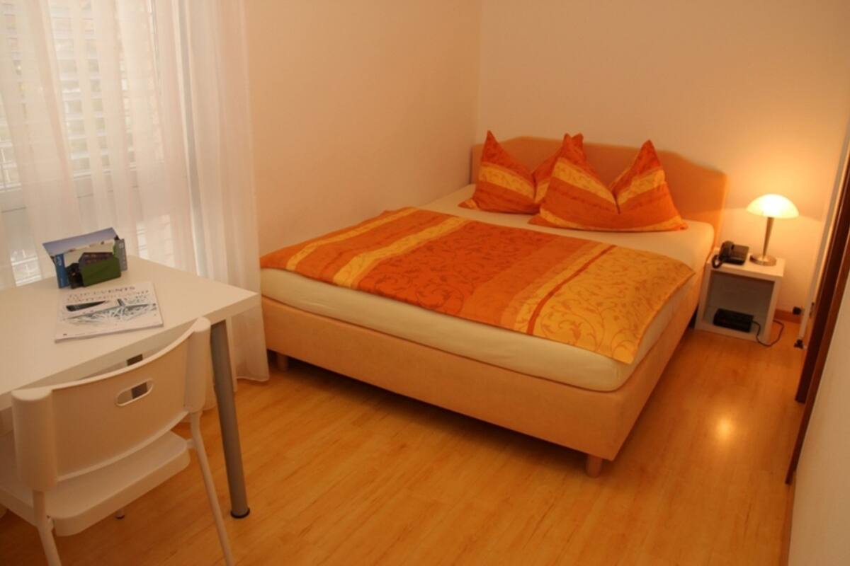 A bedroom with a bed, a desk, and a nightstand.