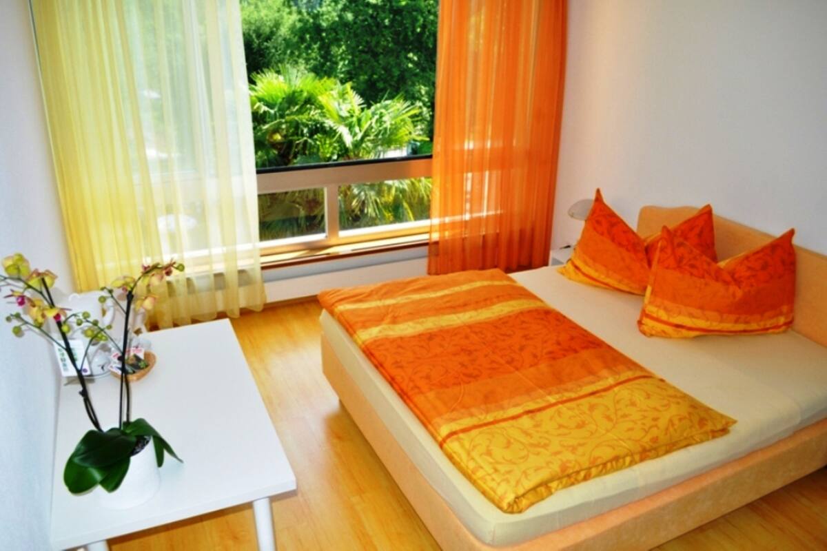 A bedroom with a bed, a small table, and a window with curtains.