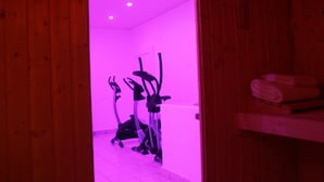 A room with wooden walls and a purple-lit ceiling. There are exercise bikes and a shelf with towels. - Rovere (Losone)