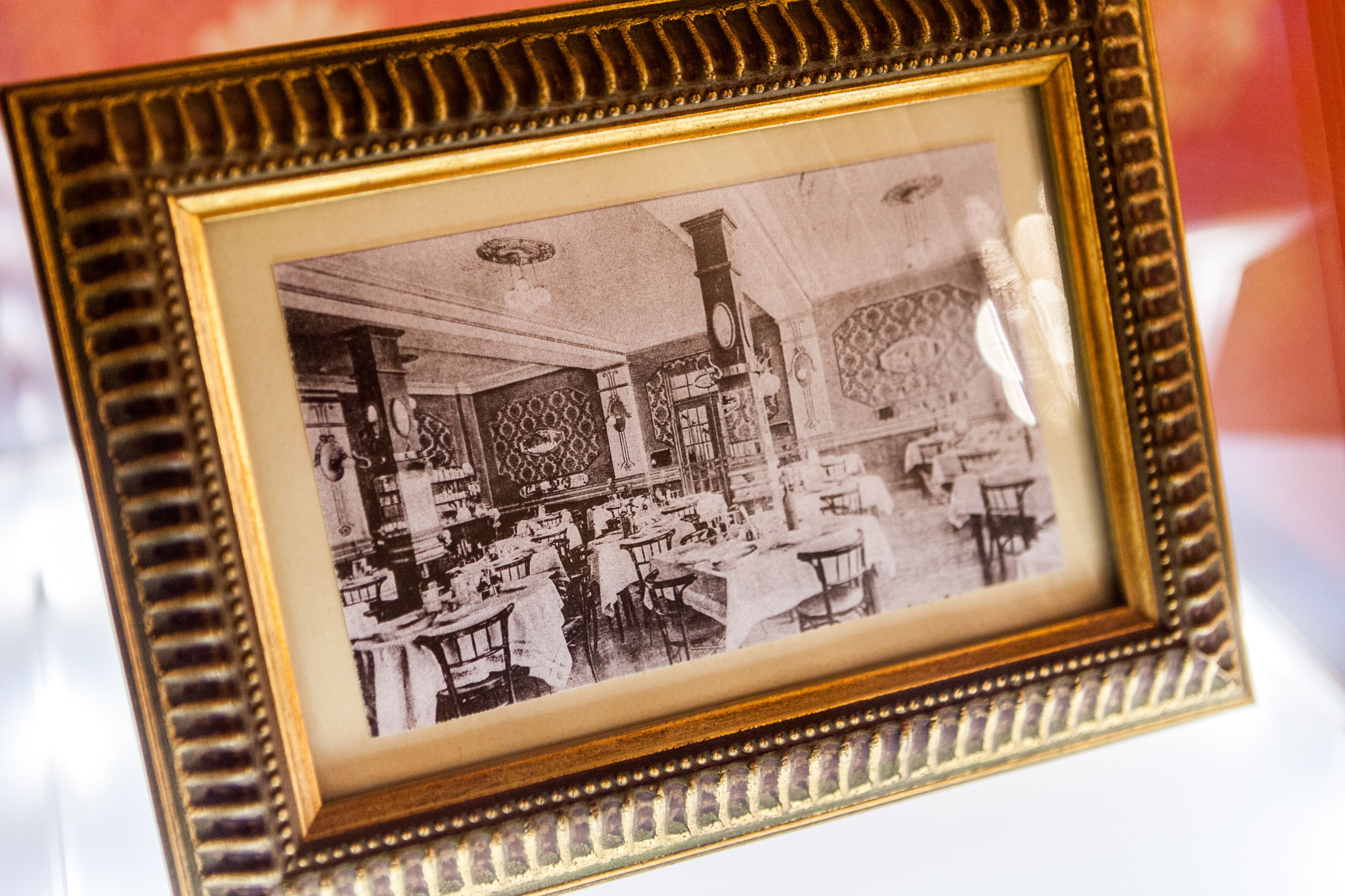 Fotografia a preto e branco de uma sala de jantar com mesas, cadeiras, um relógio e padrões nas paredes.