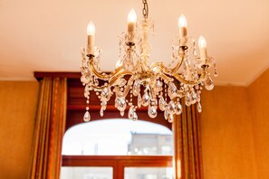 Een kroonluchter met meerdere lampen en kristallen decoraties in een kamer met een groot raam en gordijnen.