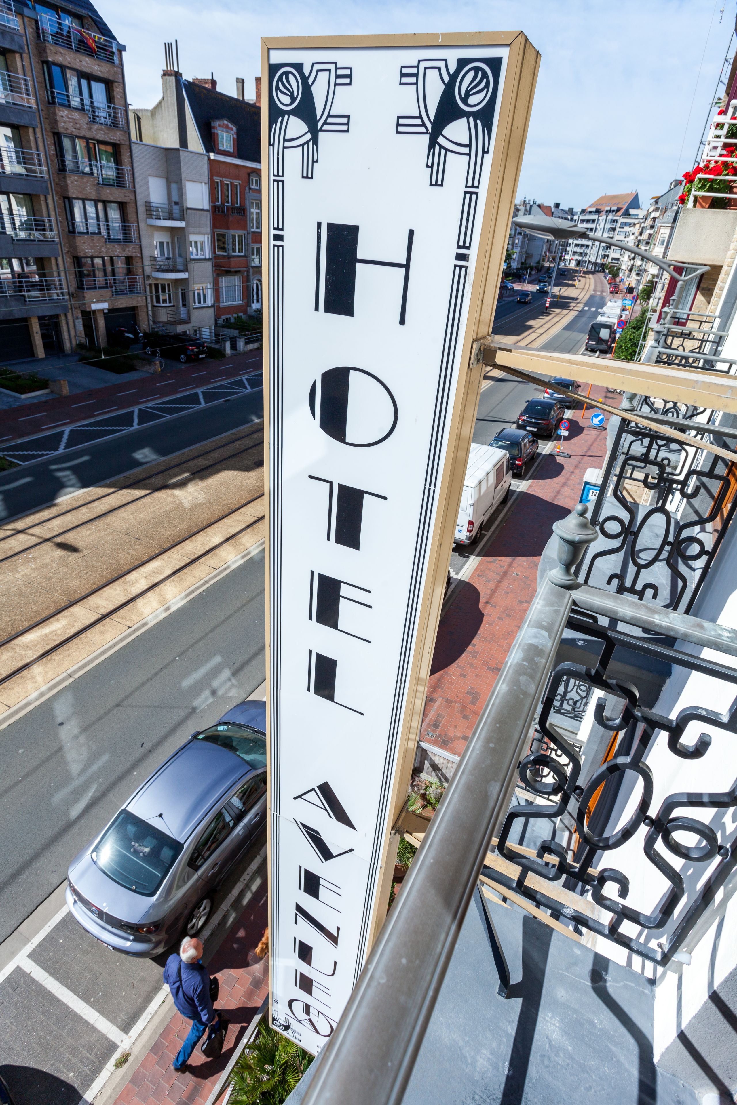 Un edificio de hotel alto y esbelto con diseño moderno, situado en una calle concurrida con coches y un tranvía.