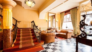 Un grand escalier avec un sol à carreaux menant à un espace de détente agrémenté d’un canapé et de fauteuils.