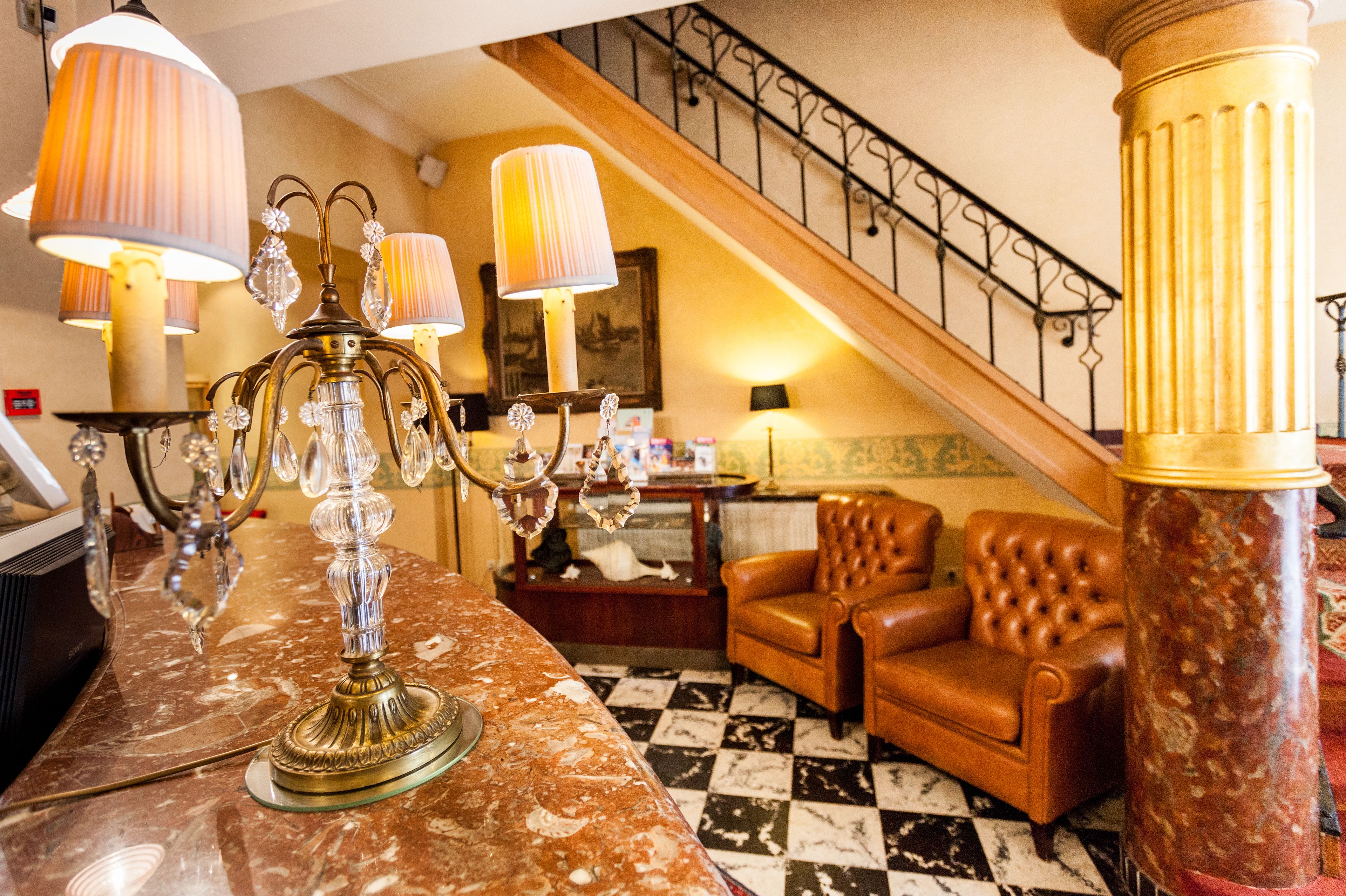 A lobby with a marble reception desk, a chandelier, a brown leather sofa, and a staircase with a railing.