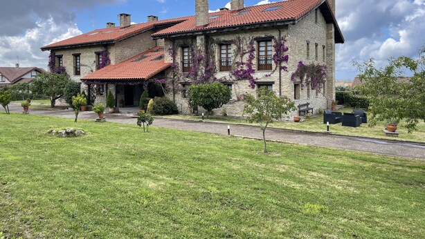 A stone building with a red-tiled roof, multiple chimneys, and a well-maintained garden with potted plants and a lawn. - Casona de Cefontes (Gijon)