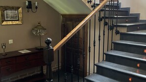 A staircase with a wooden handrail and black balusters, leading to a landing with a chandelier and a framed picture on the wall. - Casona de Cefontes (Gijon)