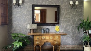 A wooden console table with a mirror above it, flanked by wall-mounted sconces. - Casona de Cefontes (Gijon)