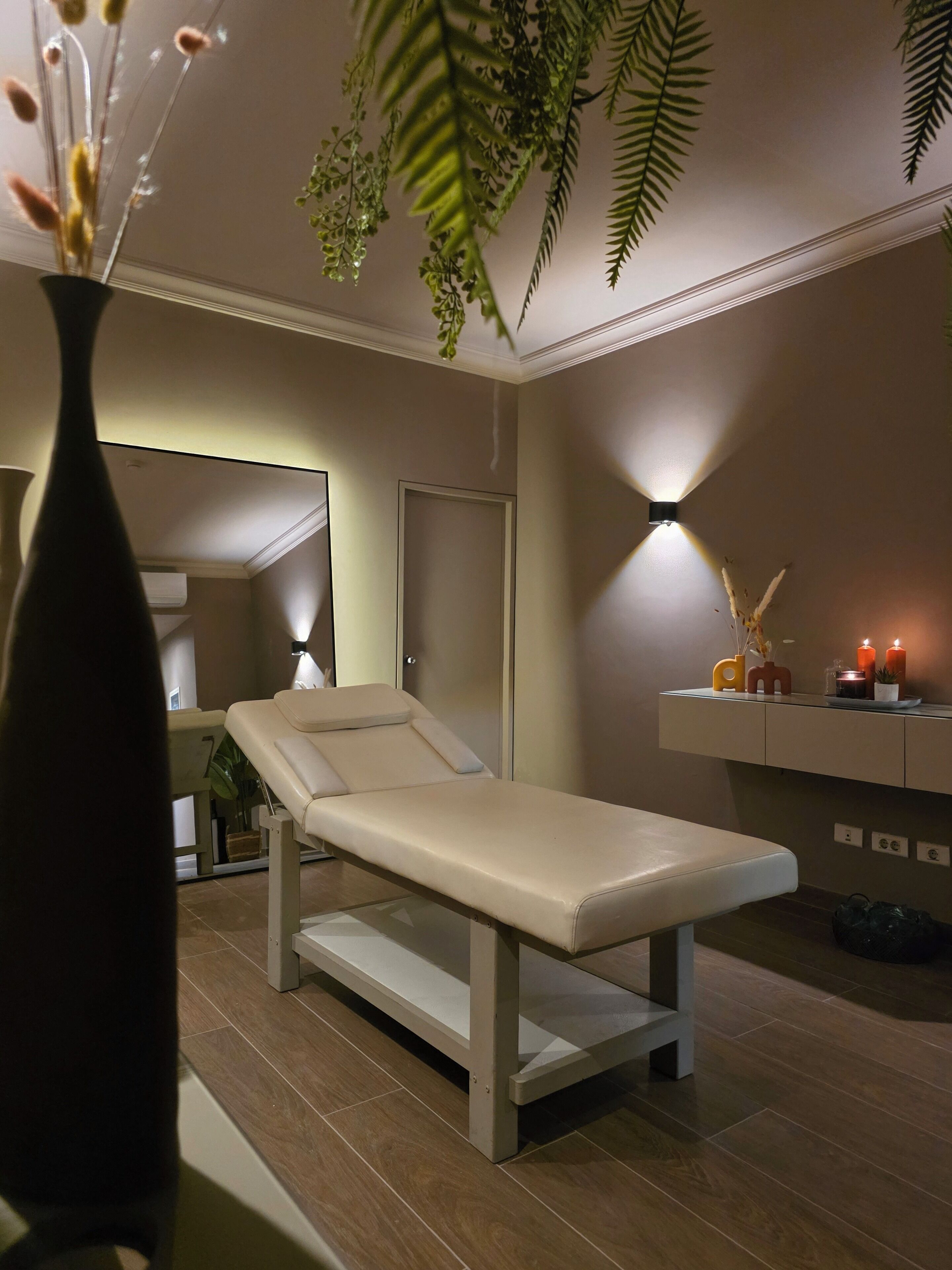 A modern examination room with a reclining chair, a wall-mounted light, and a decorative shelf with candles and plants.
