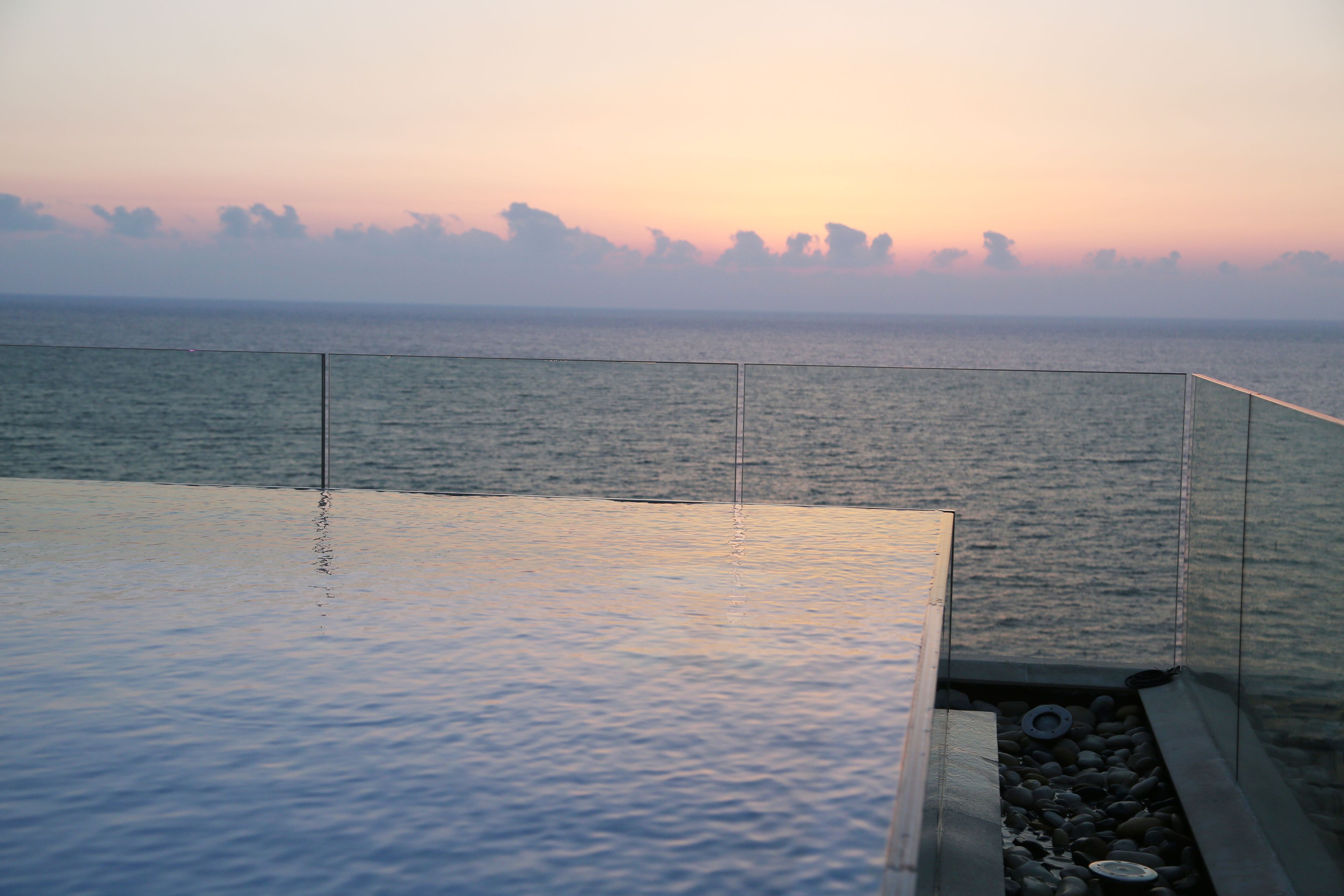 Una piscina infinita con vistas despejadas al océano y un atardecer de fondo.