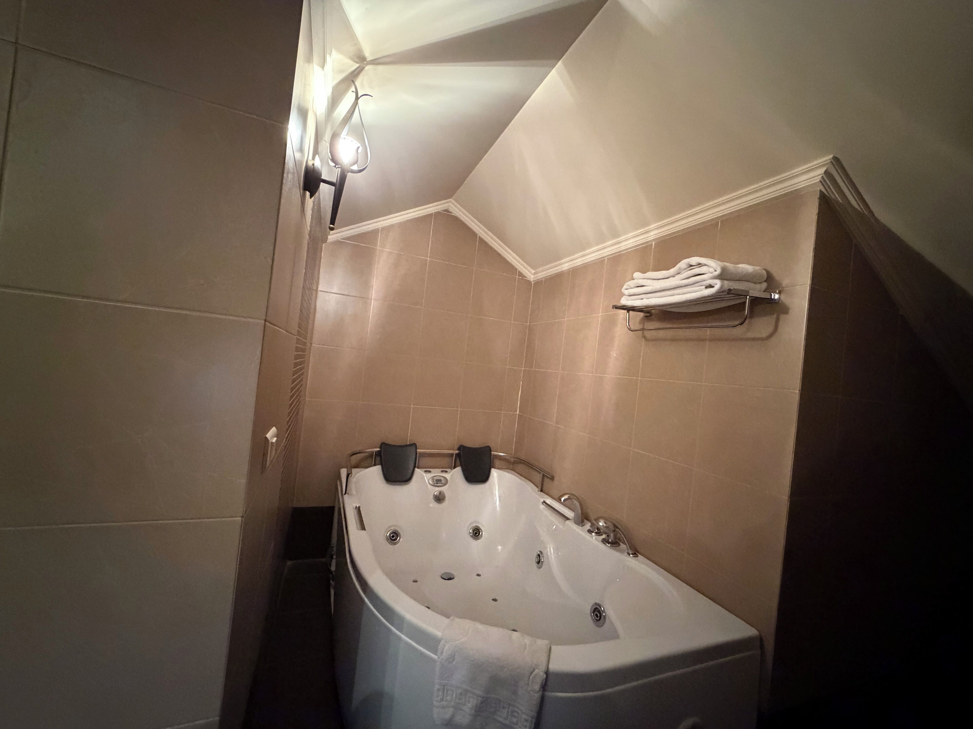 Uma casa de banho com uma banheira independente, um porta-toalhas com toalhas dobradas e uma luminária fixada na parede.