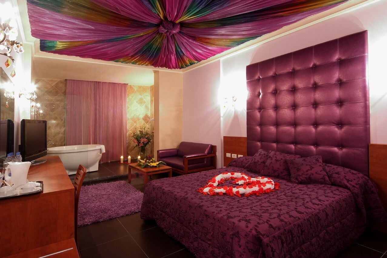 A bedroom with a tufted headboard, a bed with a rose petal arrangement, a vanity with a mirror, and a bathroom with a bathtub and shower.