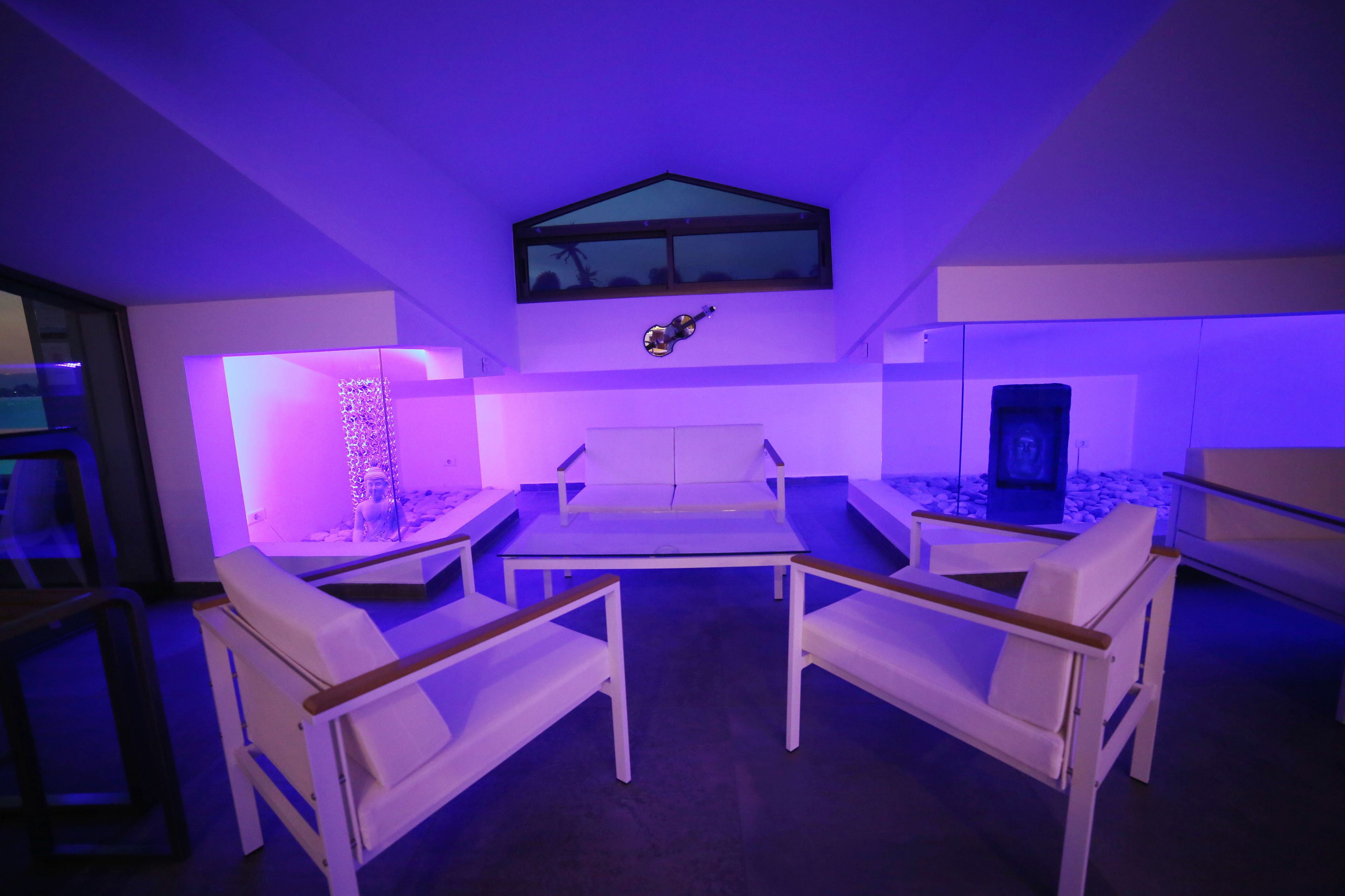 Una habitación moderna con una mesa de vidrio, sillas blancas y una guitarra en la pared.
