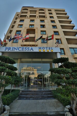 The Princessa Hotel entrance with multiple flags, a clear glass facade, and a symmetrical design.
